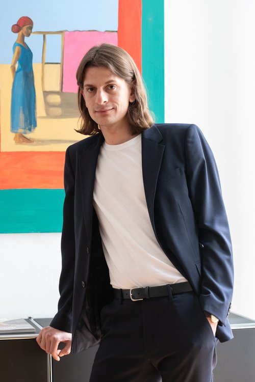 Rechtsanwalt Ansgar Gumb (Anwalt für Straf und Mietrecht) an ein Regal angelehnt. Dahinter ein Gemälde.